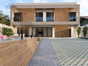 Residência contemporânea com brises verticais em madeira, grandes esquadrias de vidro, piscina e piso drenante na área externa.