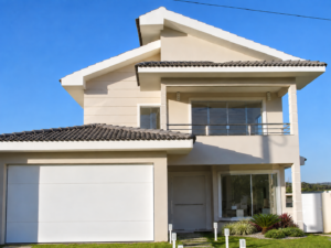 Fachada de residência contemporânea com telhado aparente, varanda no pavimento superior, grandes esquadrias de vidro, garagem e jardim frontal.