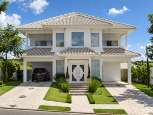 Fachada de residência de dois pavimentos com telhado aparente, entrada central, grandes aberturas de vidro, garagem lateral e paisagismo frontal.